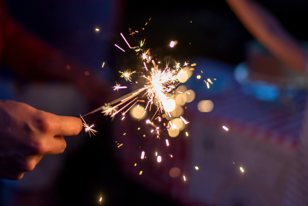 A person holds a lit sparkler, with bright sparks and bokeh lights illuminating the dark background. The scene captures a sense of celebration and joy, reminiscent of a veterinarian's heartfelt dedication as they celebrate another successful day caring for beloved animals.